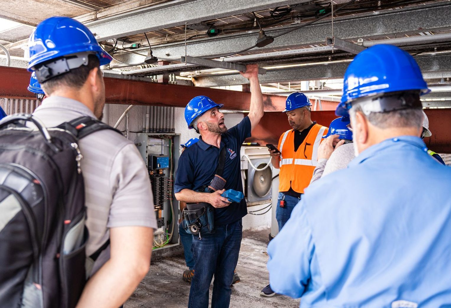 A group of men wearing hard hats and vests are standing in a room.
