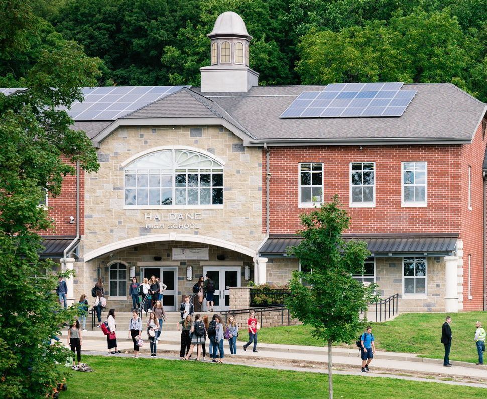 A group of people are walking in front of a large brick building with solar panels on the roof.