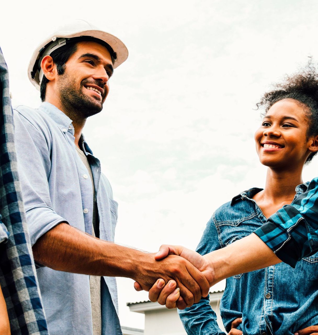 A man in a hard hat shakes hands with a woman in a plaid shirt