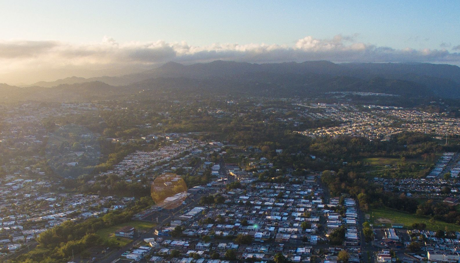 Vista aérea de una ciudad densamente poblada con casas y edificios bajo un cielo brumoso y montañas distantes.