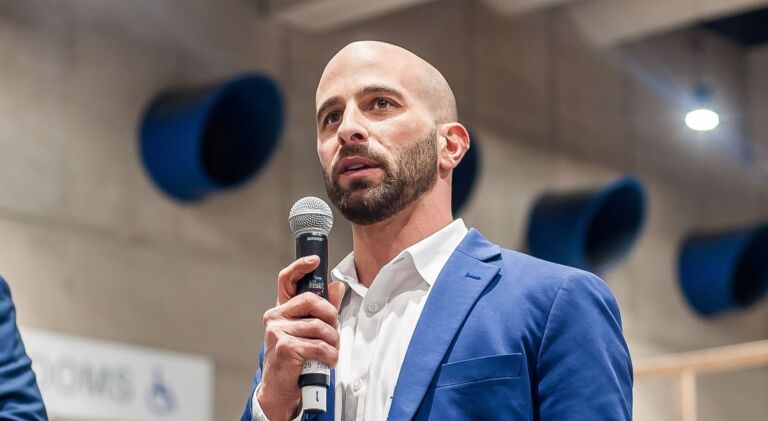 A bald man in a blue suit is holding a microphone.