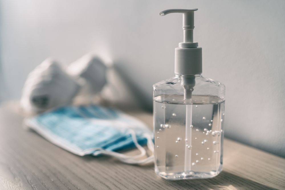 A bottle of hand sanitizer is sitting on a wooden table next to a mask.