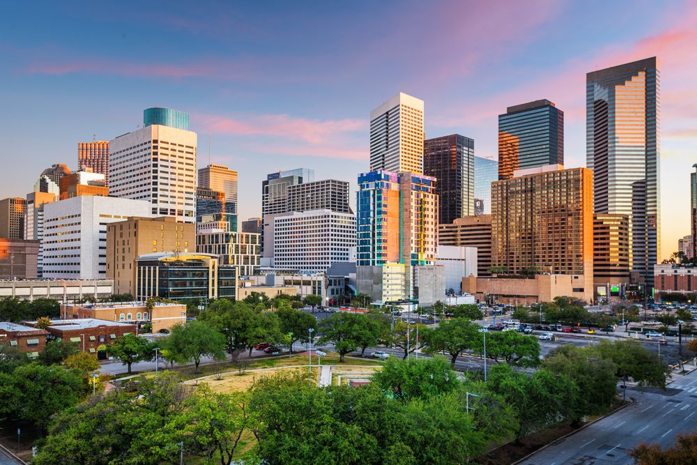 An aerial view of the Houston skyline at sunset with trees in the foreground.