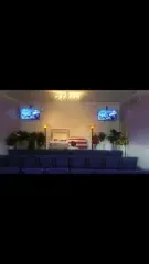 A church altar with a casket draped in a flag, two TVs, and floral arrangements.