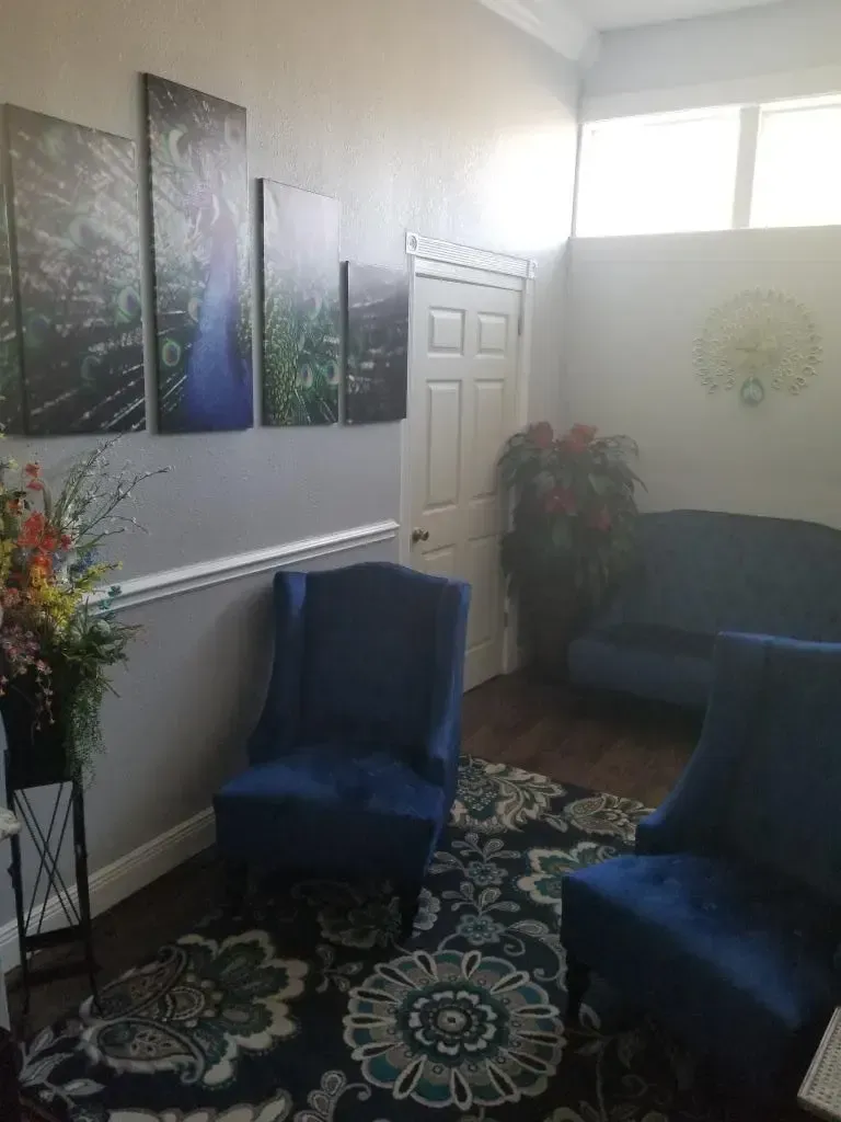 Blue chairs and sofa in a waiting area with floral artwork, door, and a rug.
