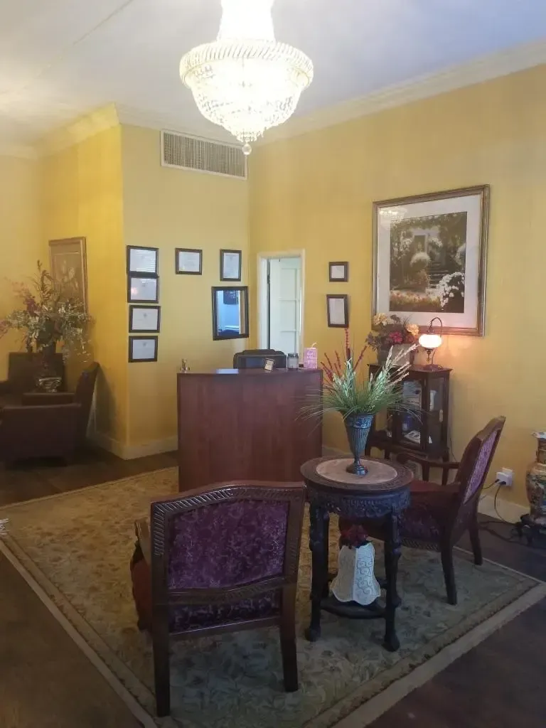 Reception area with yellow walls, chandelier, dark wood desk, chairs, and framed artwork.