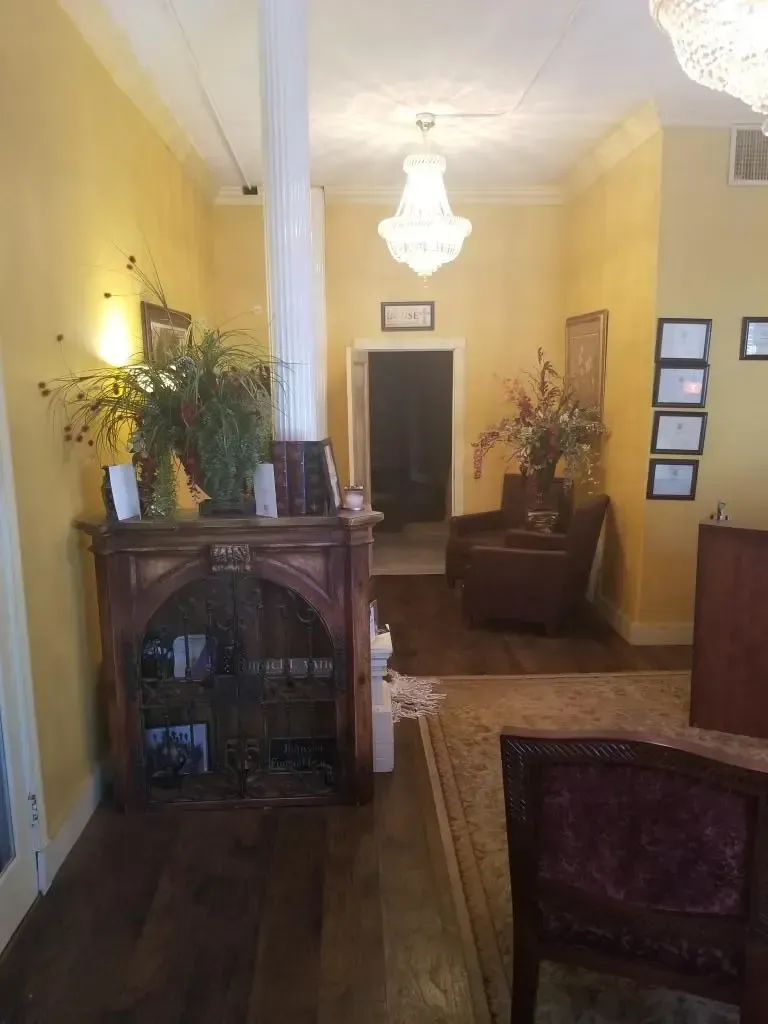 A hallway with yellow walls, chandelier, dark wood furniture, and an open doorway.
