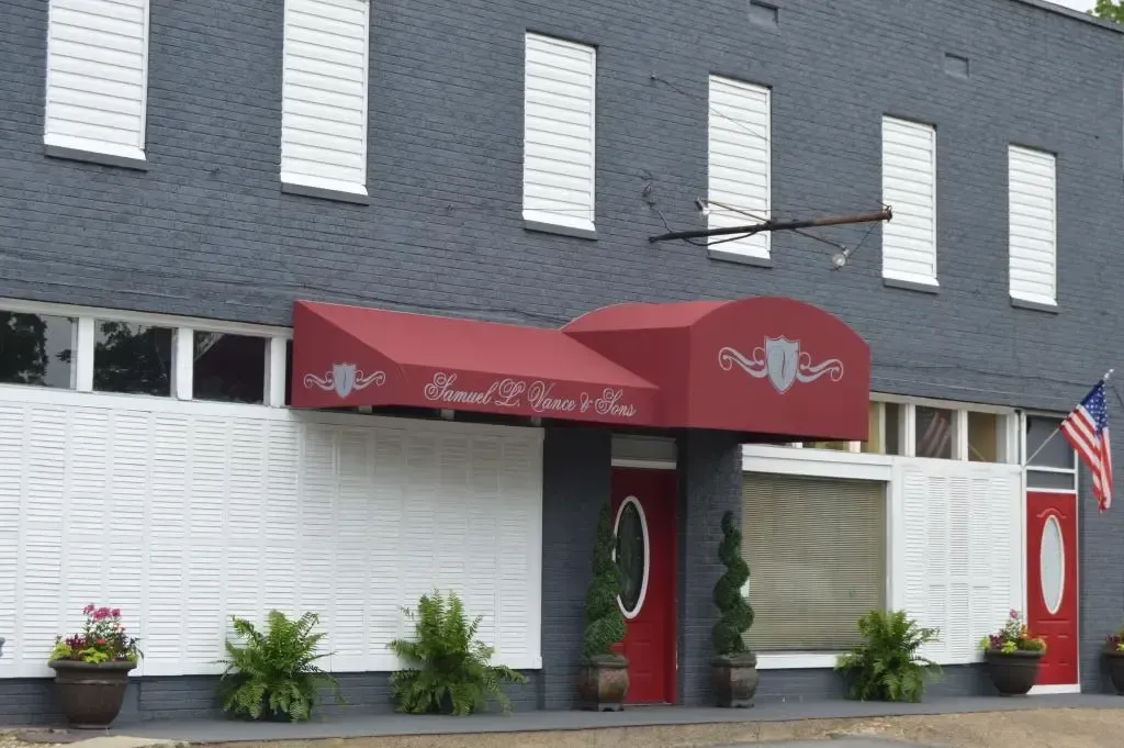 Red awning over a building entrance with dark gray facade and white block wall. American flag.