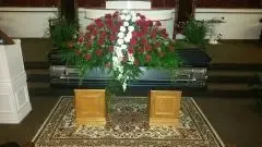 A casket with floral arrangement inside a church. Two wooden pedestals sit in front of it.