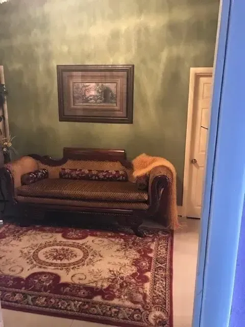 Living room with ornate sofa, oriental rug, and landscape art on a green wall.