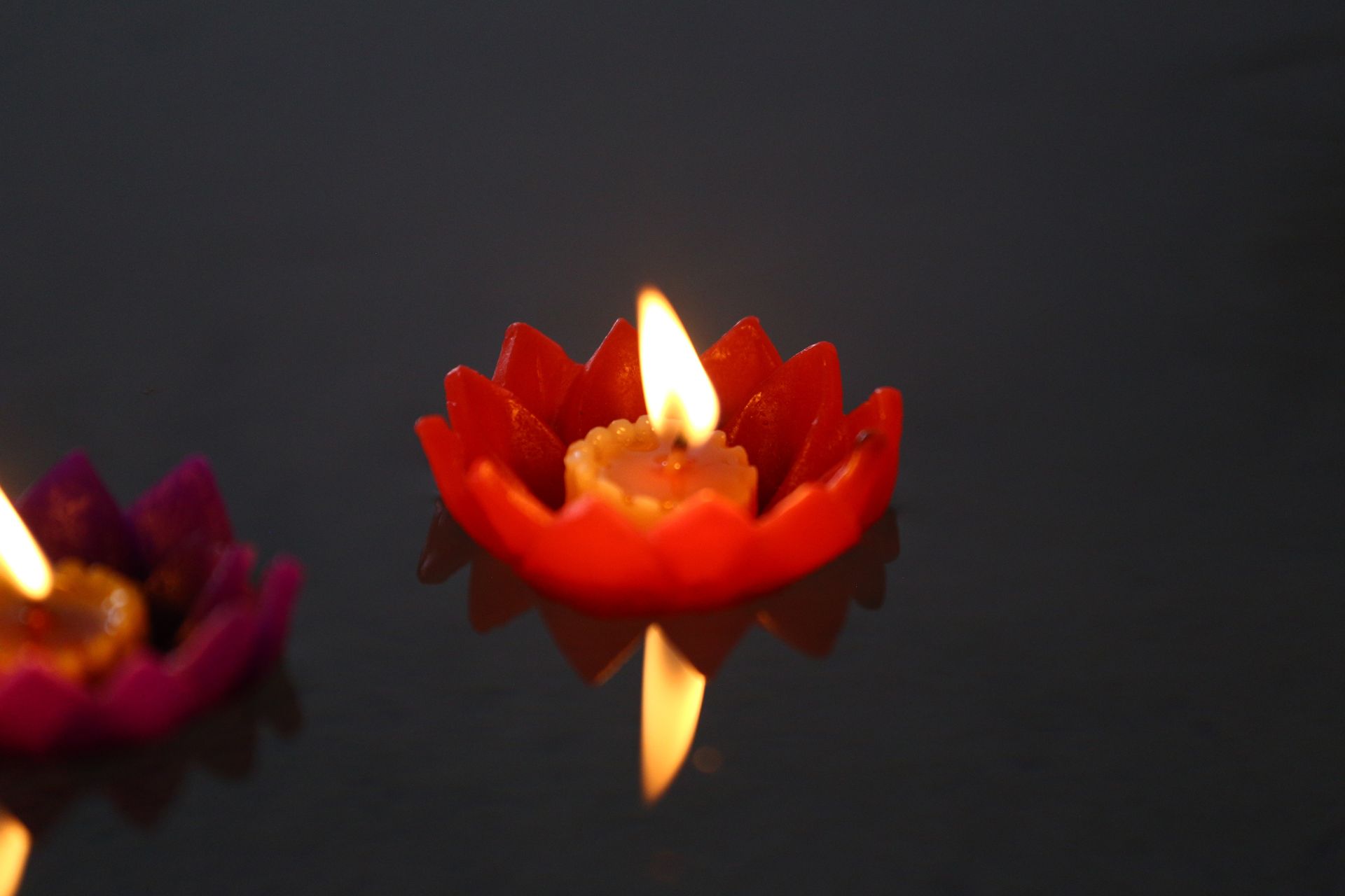 Red lotus-shaped candle floating on dark water, flame lit.