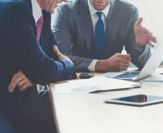Two men in suits and ties are sitting at a table with a laptop.