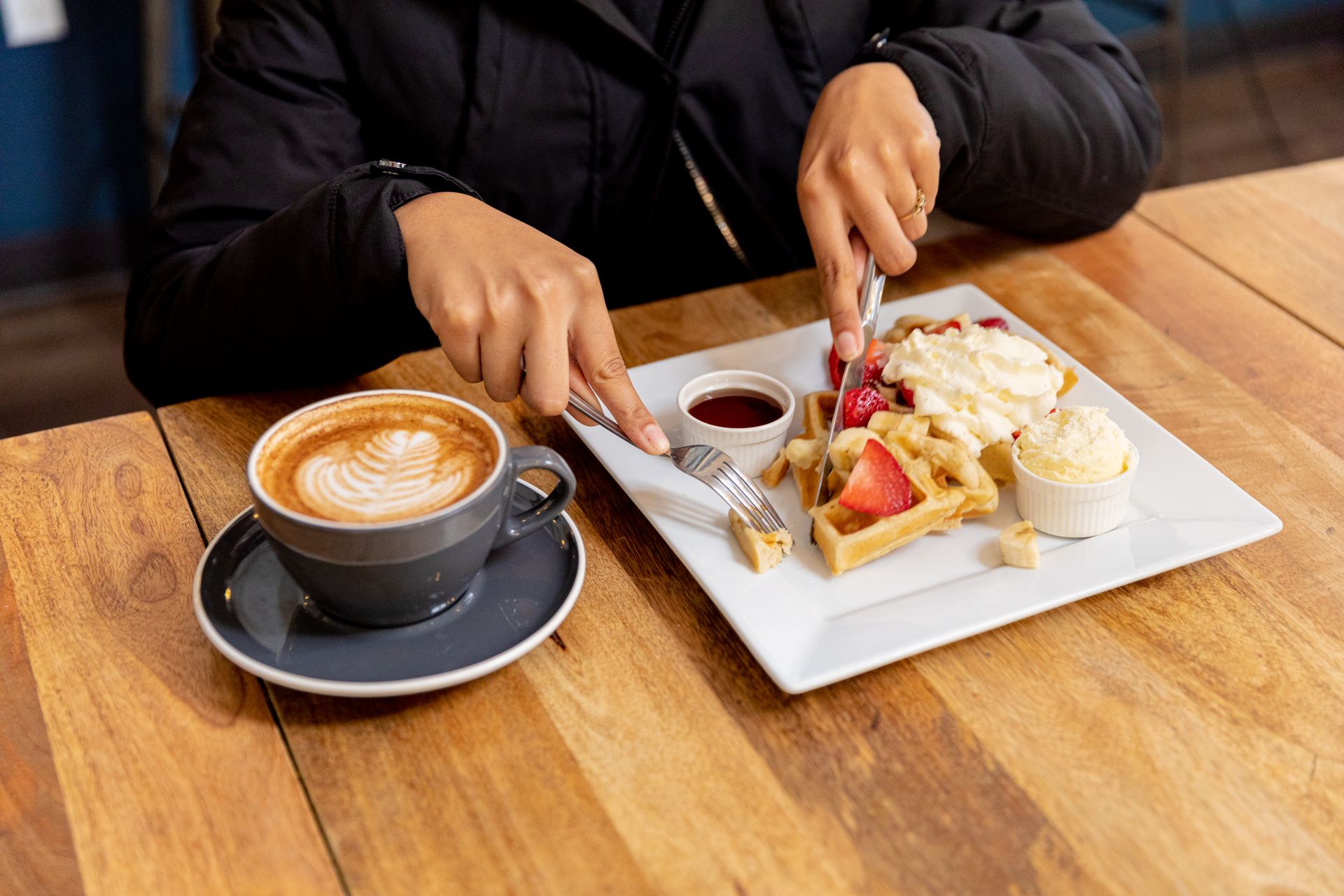 A person is sitting at a table with a plate of food and a cup of coffee.