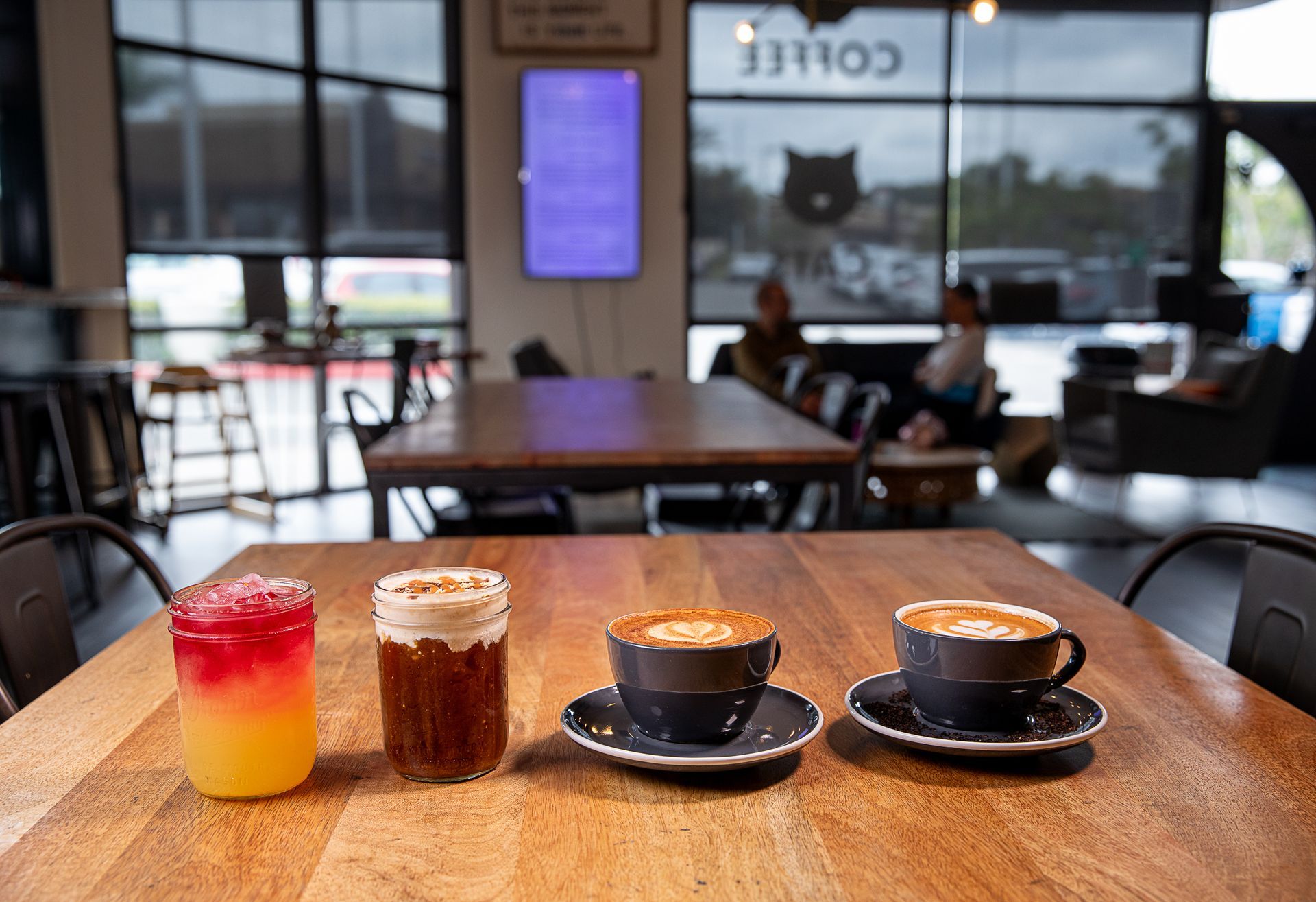 Three cups of coffee are sitting on a wooden table in a restaurant.