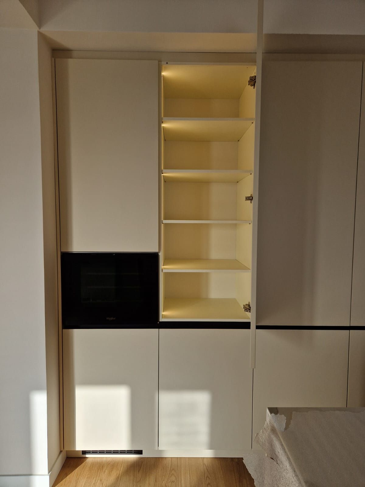 Un mobile bianco con una porta nera e degli scaffali in una stanza.