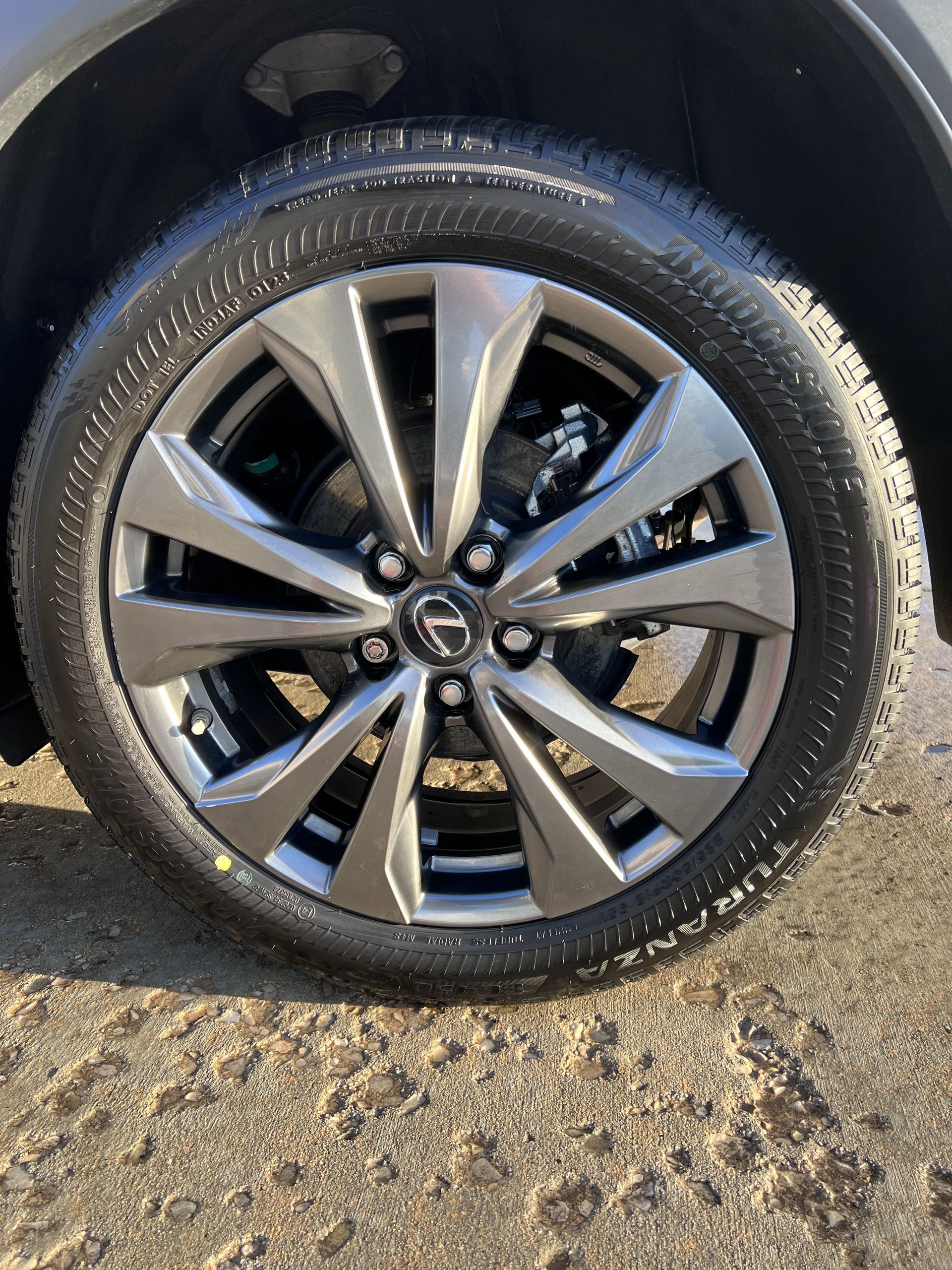 Car tire with a gray rim and a black tire on a sandy surface.