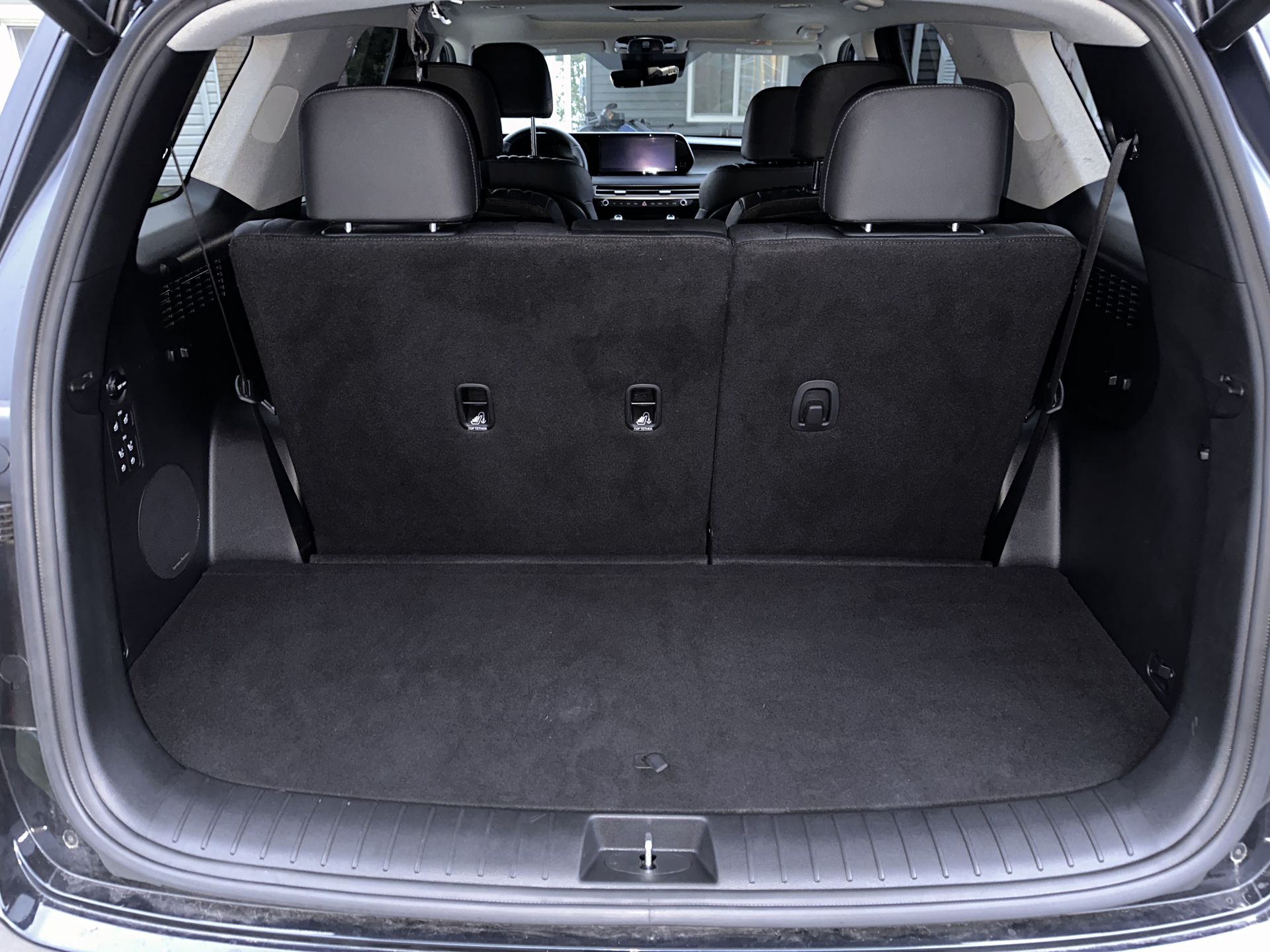 Empty black car trunk with folded-down seats, black carpet, and a storage space.