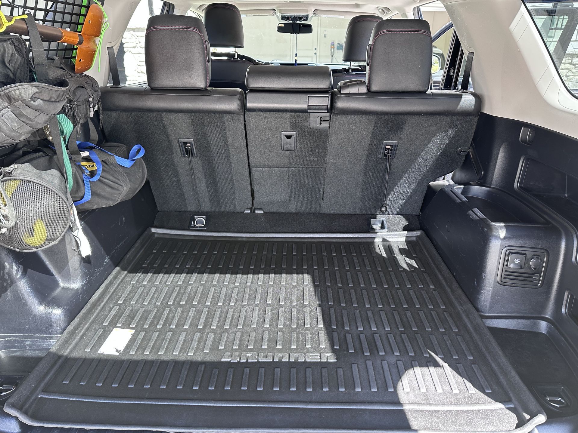 Interior of a Toyota 4Runner cargo area with black floor mat, rear seats up, and some gear stored.