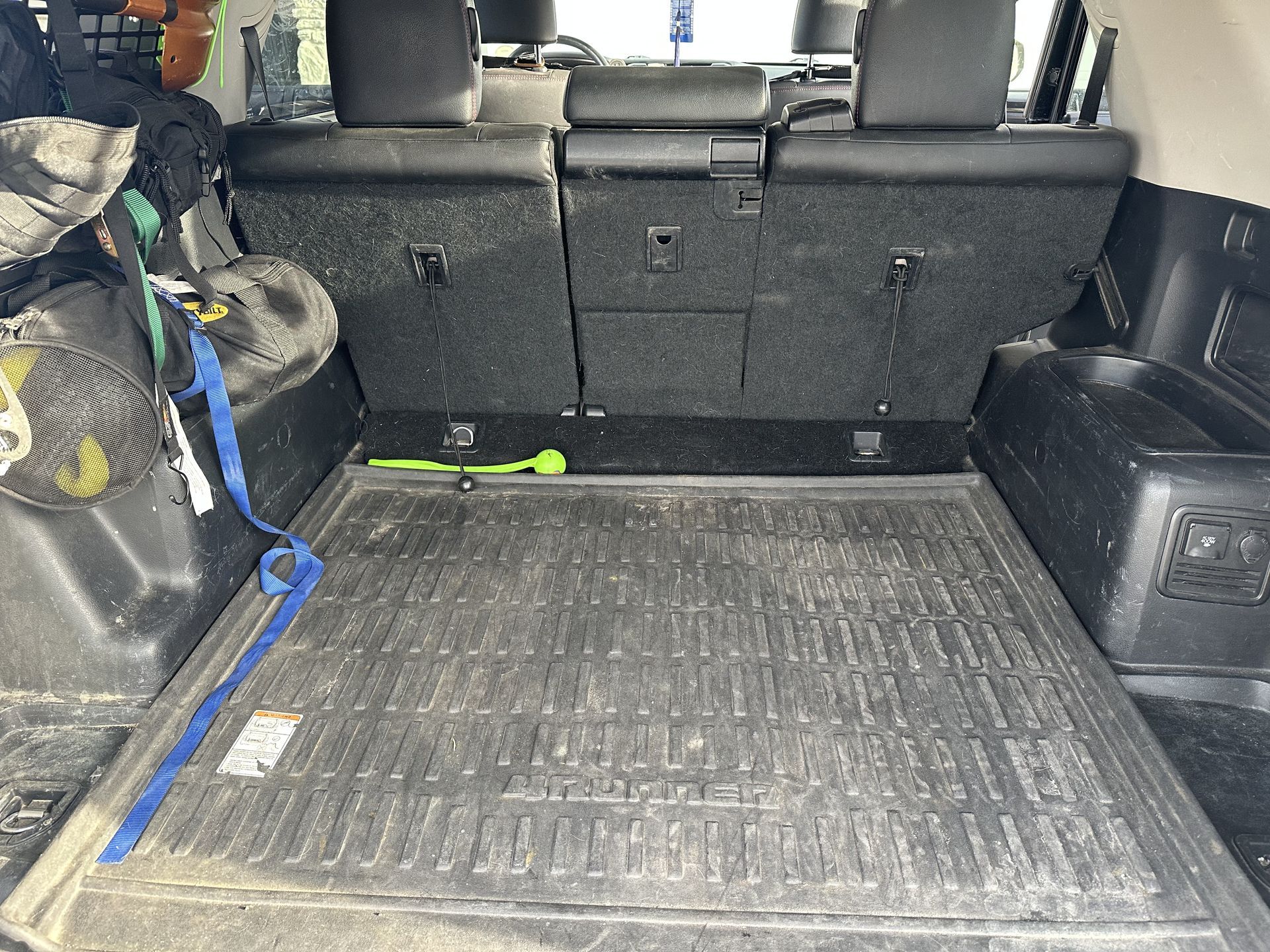 Back of a car with a black rubber mat. Dirty, with a blue strap and some items on the sides.