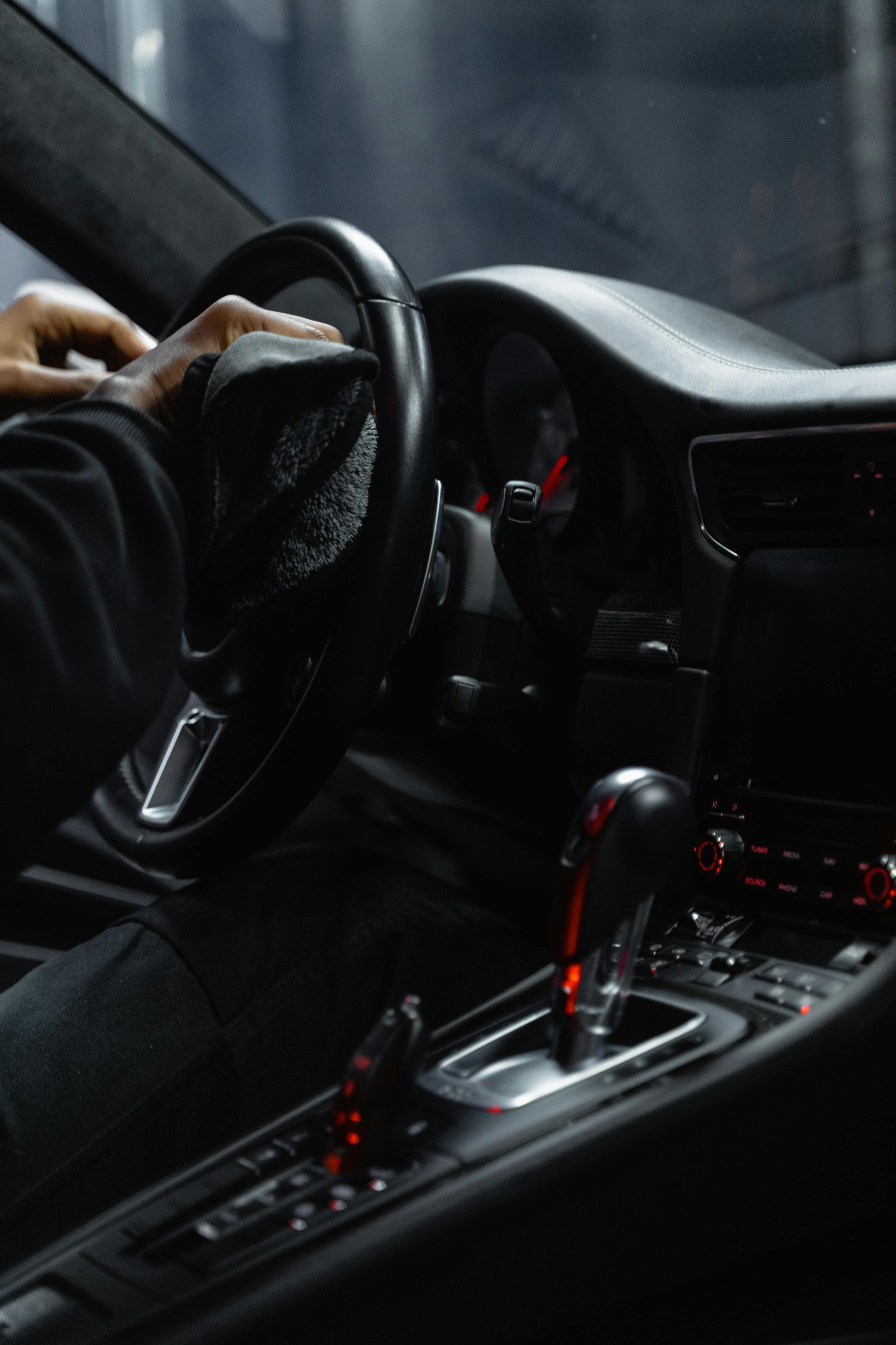 Person wiping the steering wheel of a black car's interior with a dark cloth; close-up.