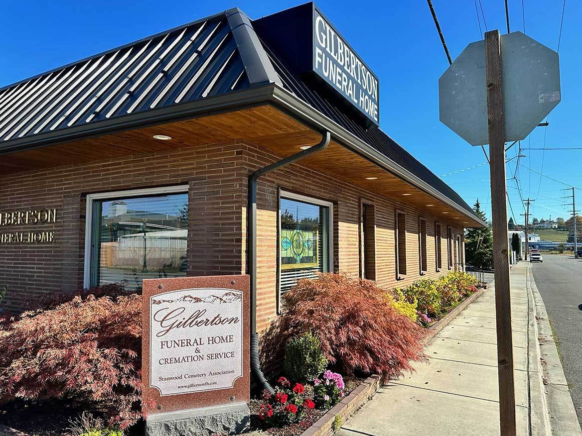 Brick building with a sign for Gilbertson Funeral Home, stop sign on the sidewalk.