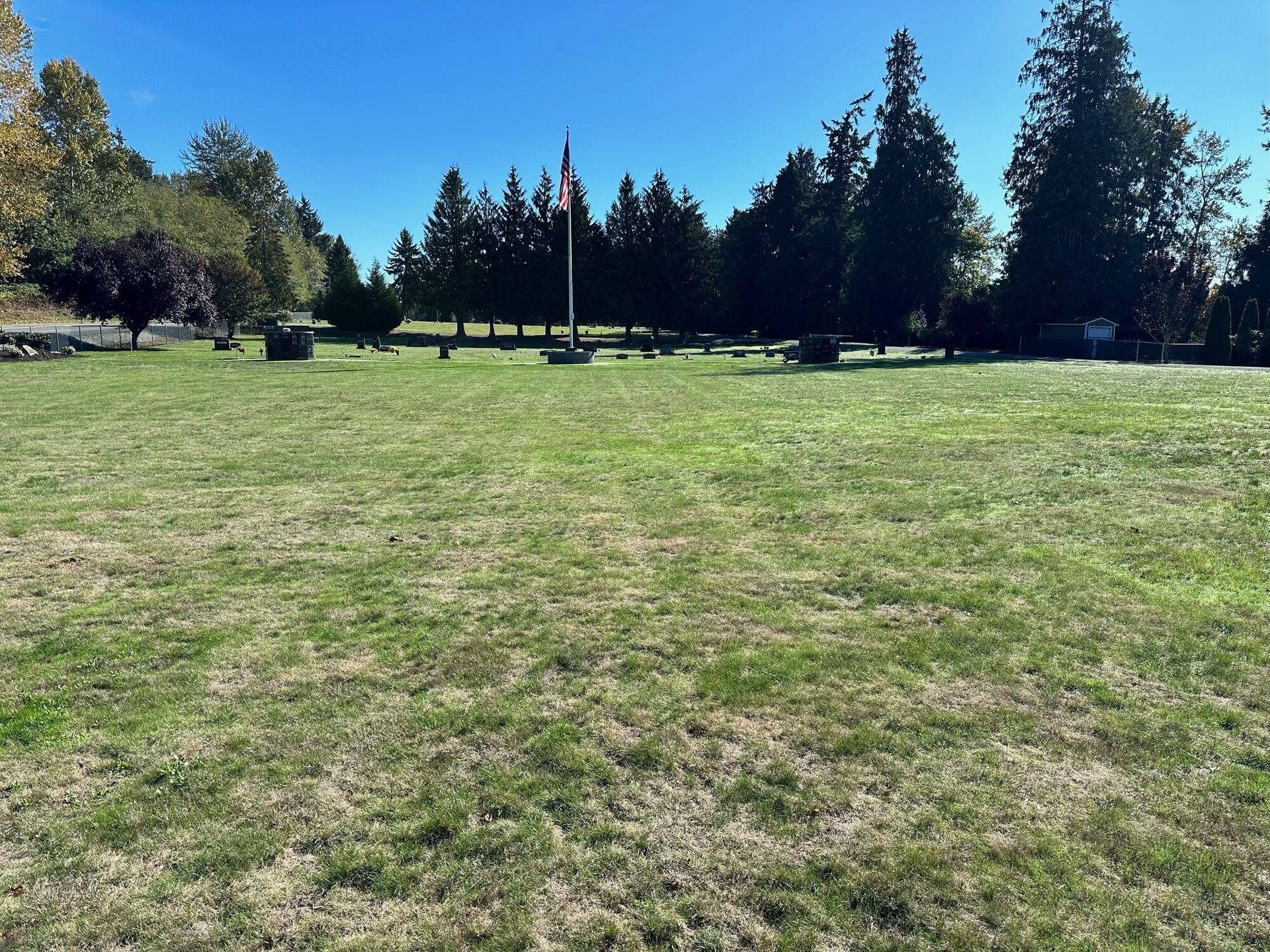 Green grassy cemetery with headstones, American flag, trees, and blue sky.