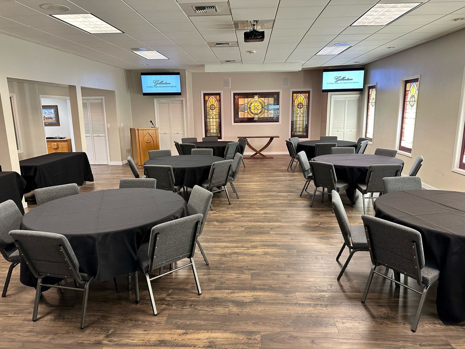 Meeting room with round tables, chairs, and two TVs. The room is well lit.