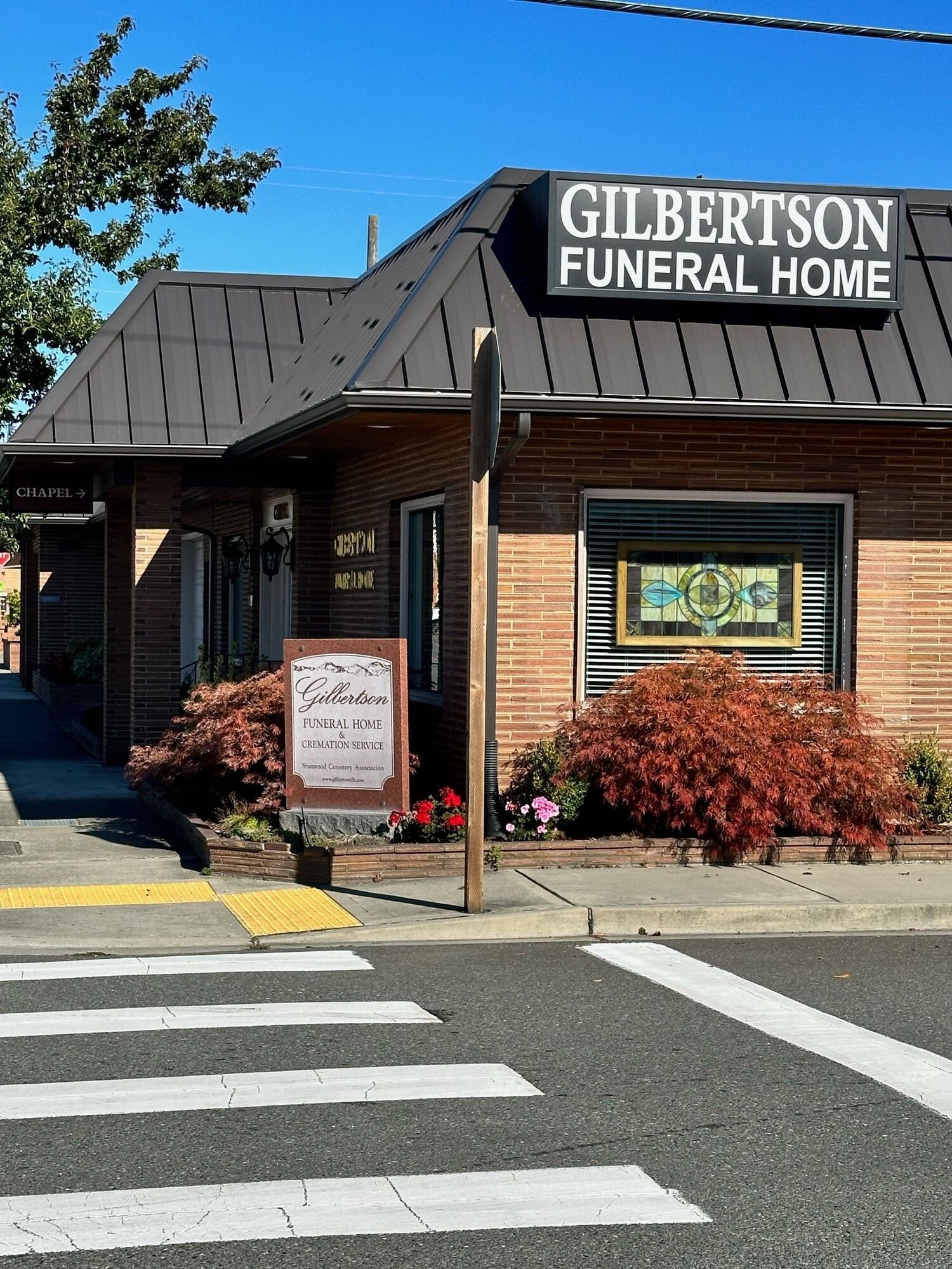Gilbertson Funeral Home, small brick building with sign on a sunny day. A crosswalk is in the foreground.