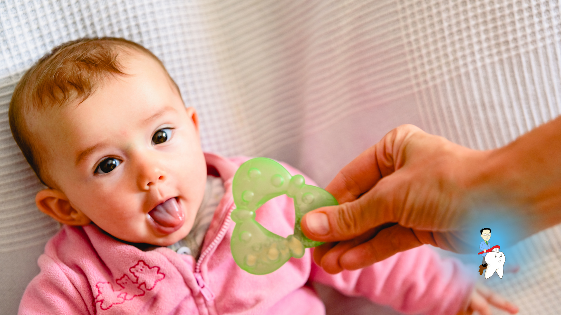 A baby is laying in a crib and a person is holding a teething ring.