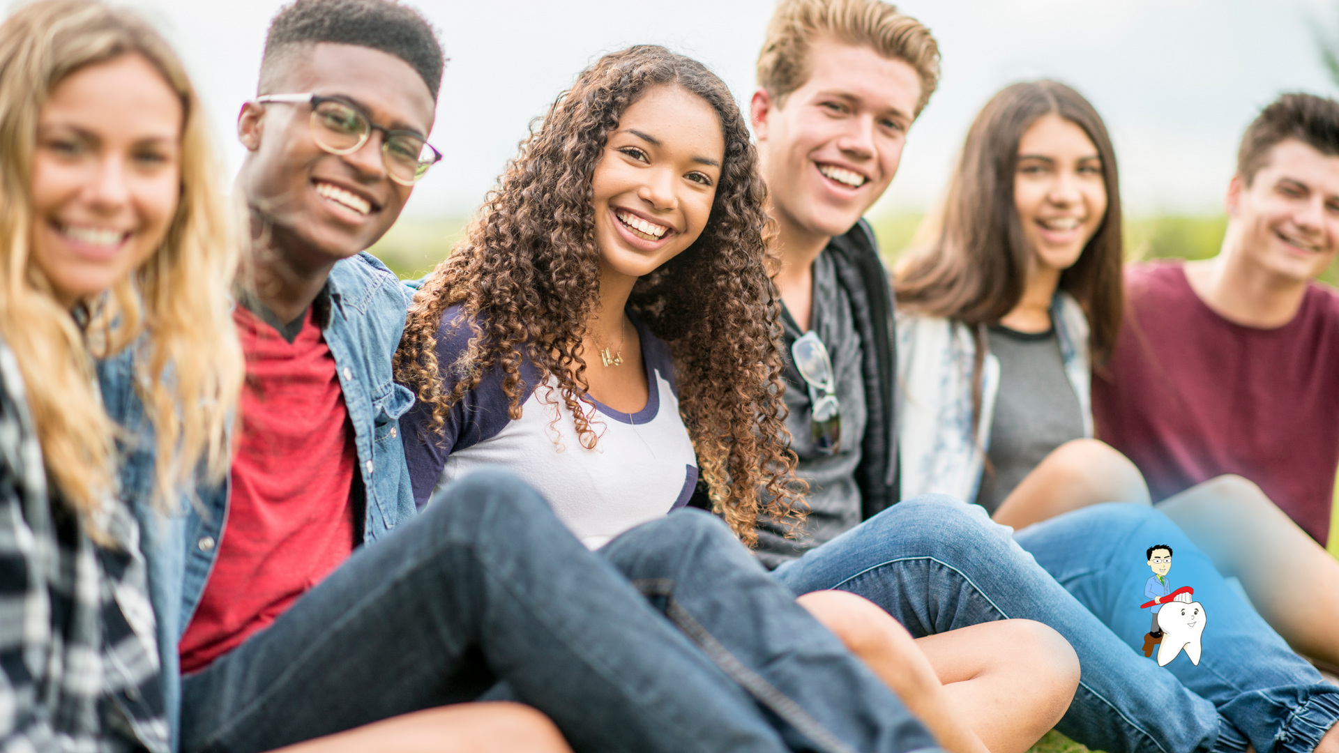 A group of young people are sitting on the grass and smiling for the camera.