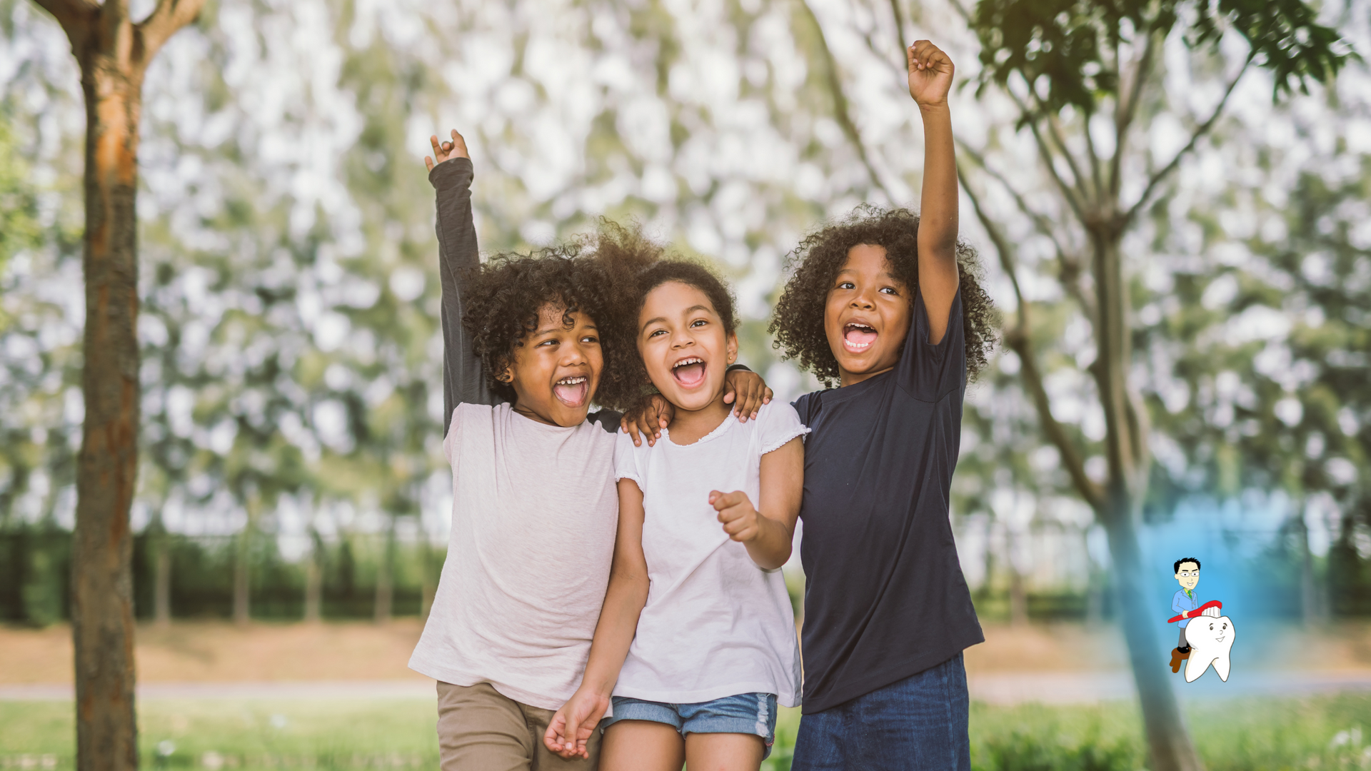 Three children are standing next to each other in a park with their arms in the air.