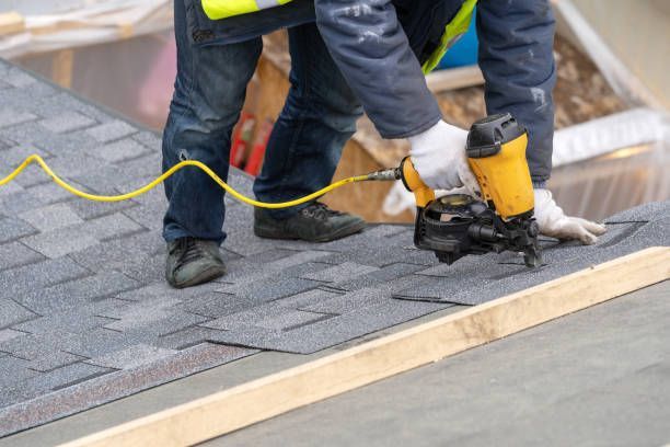Contractor installing asphalt roof shingles with nail gun during residential roof construction.