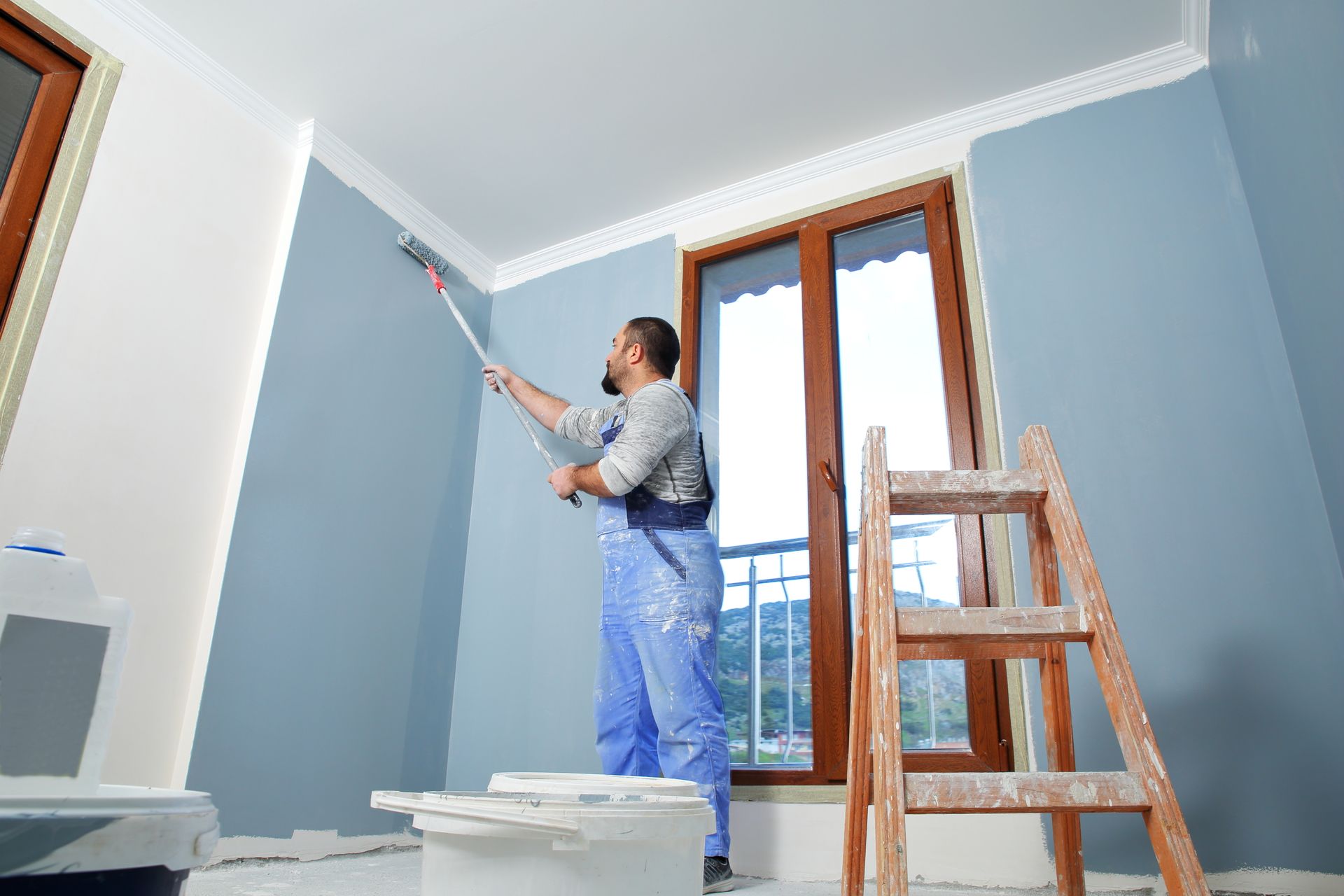 A Man Is Painting A Wall In A Room With A Roller — Huron, SD — Shaddai Construction