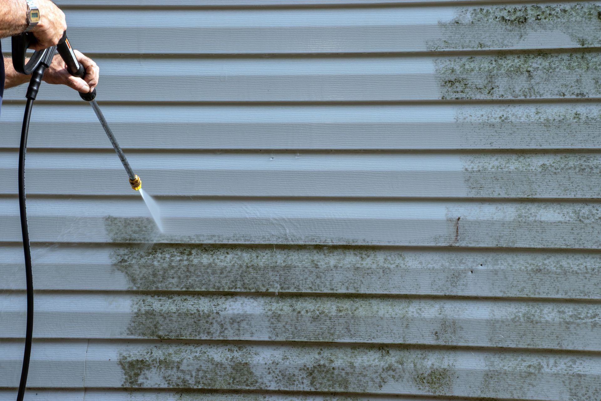A Person Is Cleaning The Side Of A House With A High Pressure Washer — Huron, SD — Shaddai Construction