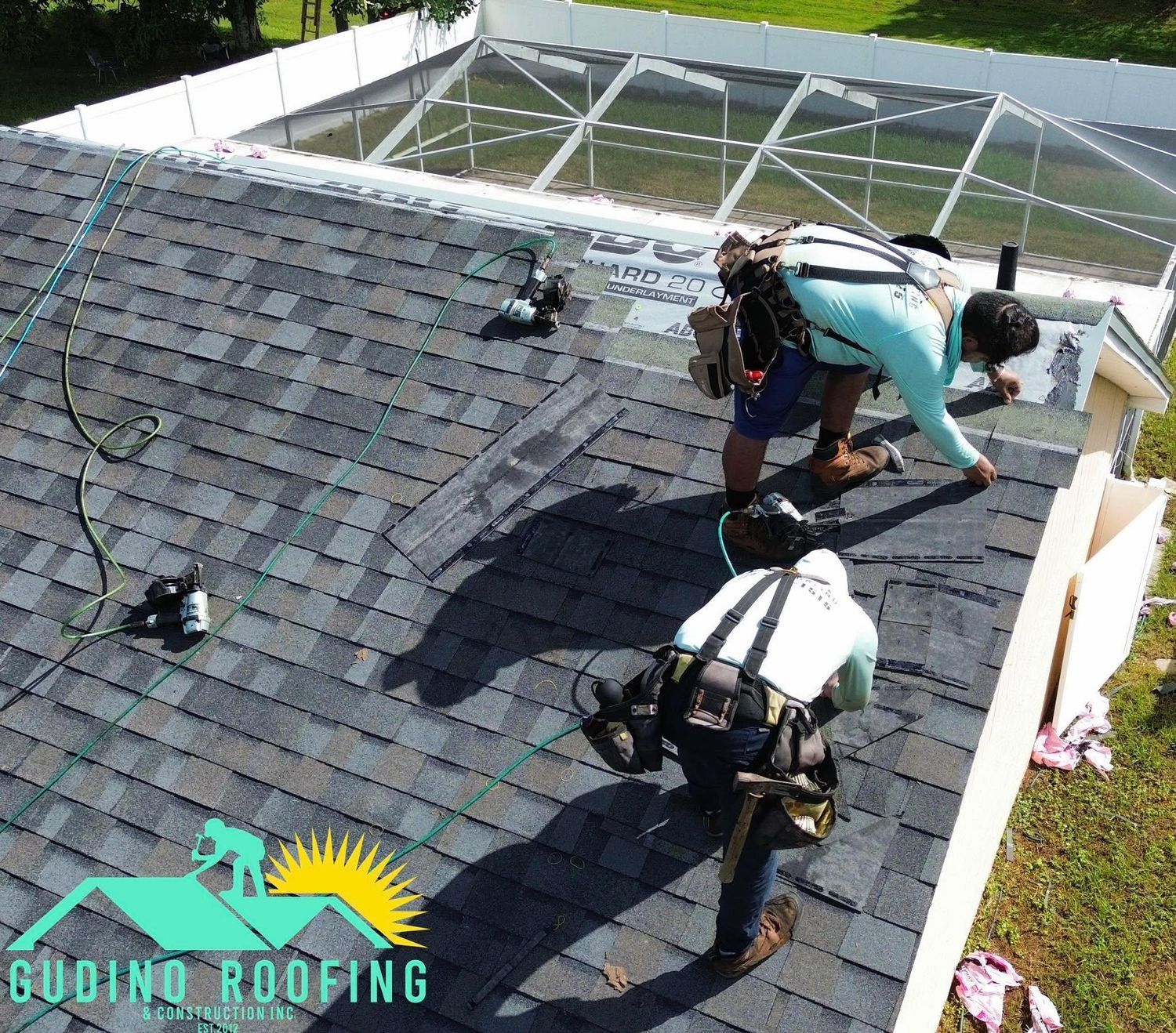 Roofers on a shingled roof installing materials with safety harnesses and tools.
