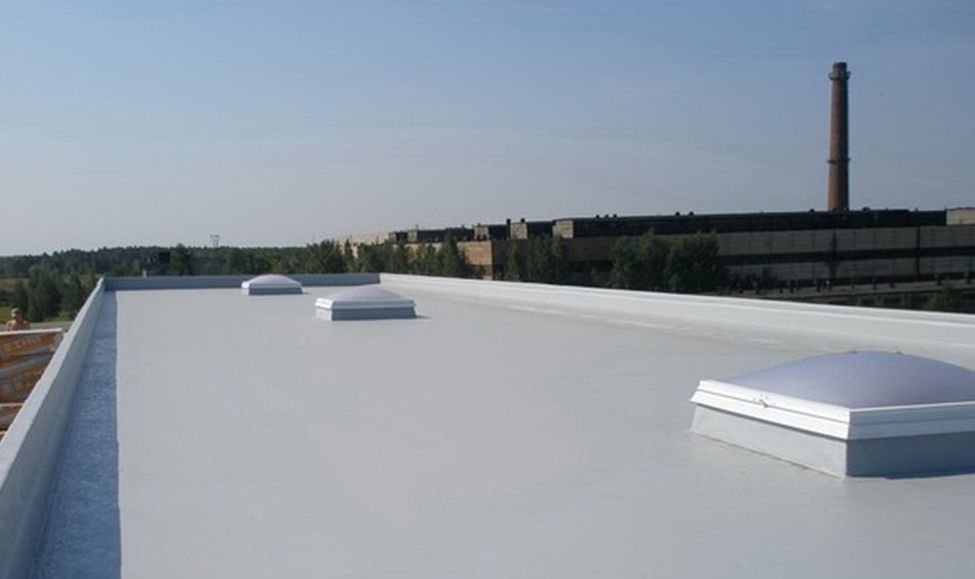Flat white rooftop with vents, overlooking industrial buildings and a tall smokestack under a clear sky
