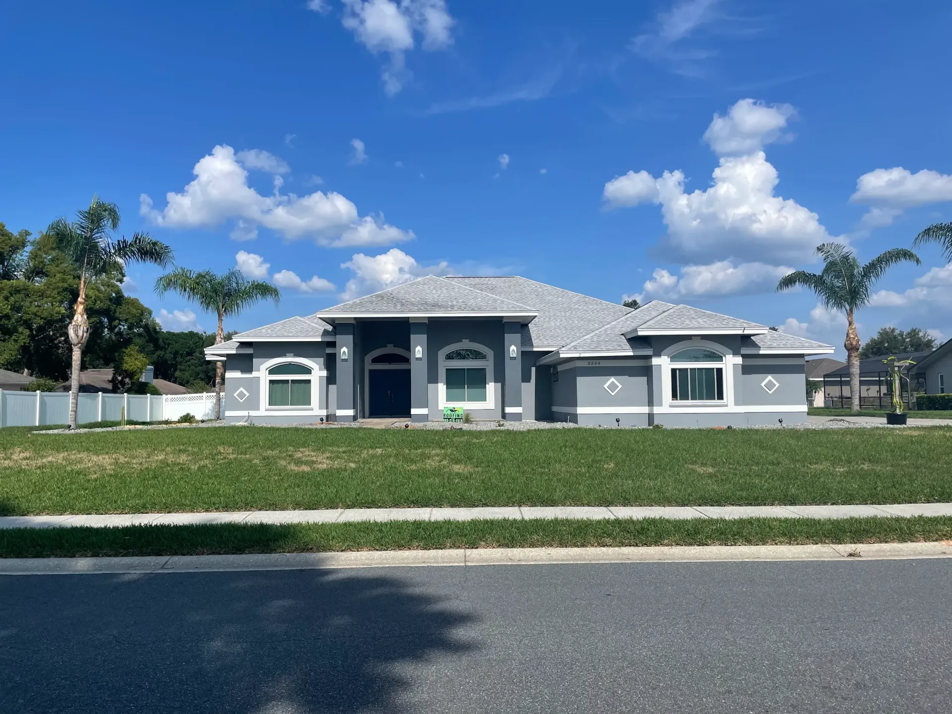 Single-story gray house with white trim, front lawn, and blue sky with clouds