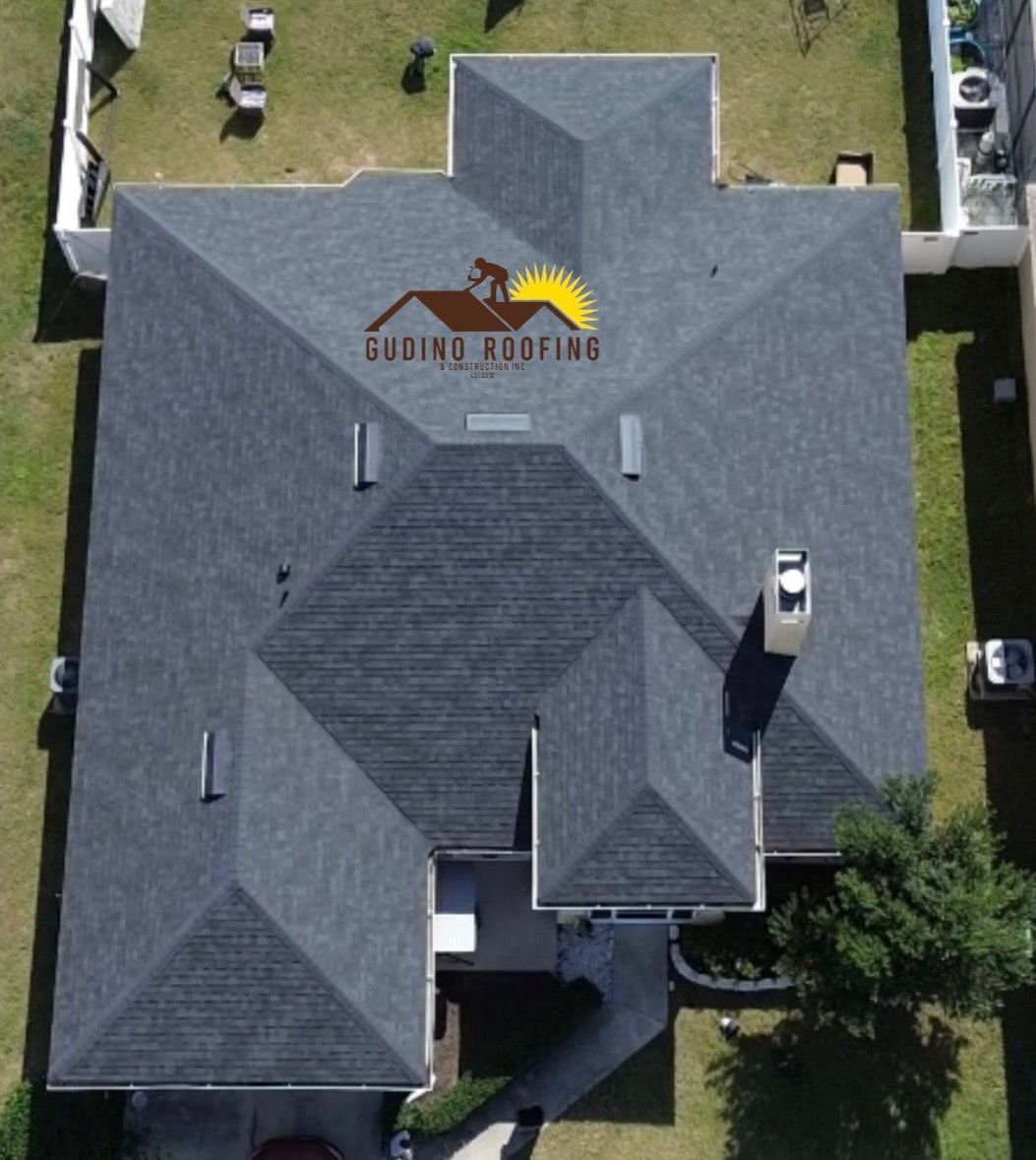 Aerial view of a gray-roofed house with a central entryway and surrounding lawn.