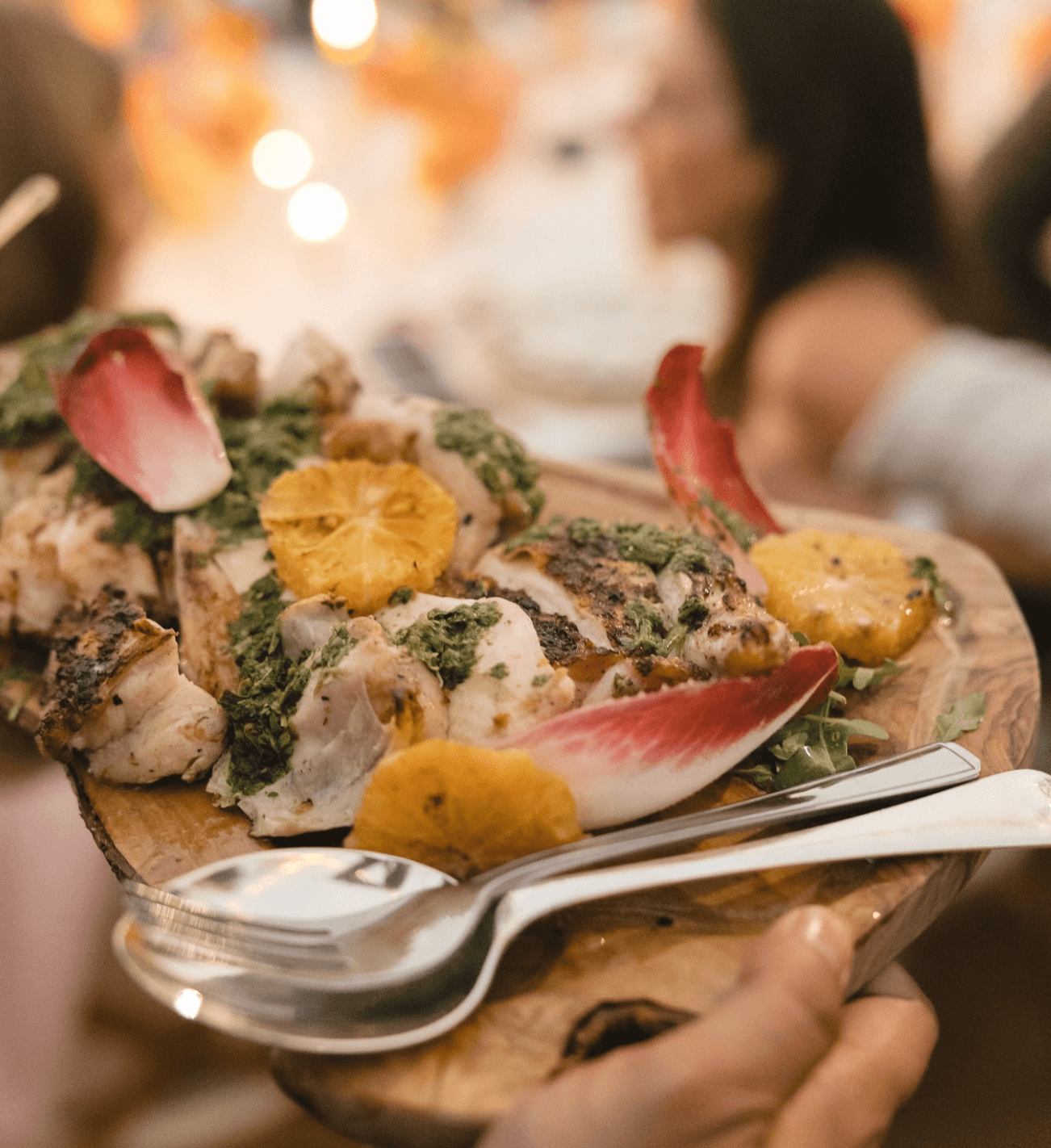 A person is holding a plate of food with a fork and spoon on it.