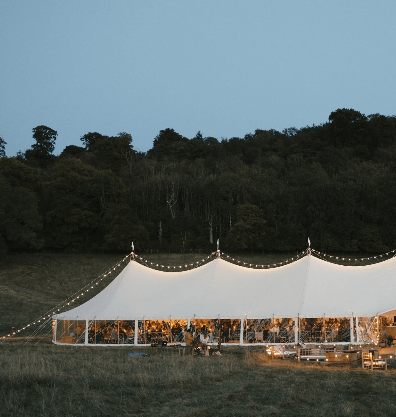 A large white tent is lit up in the middle of a field