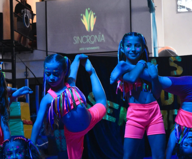 Jóvenes artistas vestidos con trajes de neón realizando poses acrobáticas en el escenario.