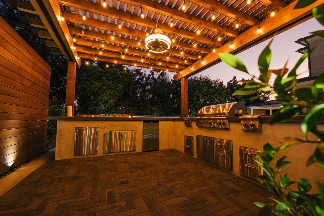 Outdoor patio with string lights, a grill, and a wooden pergola; evening setting.