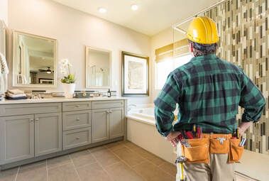 Maple Ridge Handyman Service provider wearing a yellow hard hat and orange tool belt looking at a bathroom renovated. The bathroom has a grey vanity and yellow paint on the walls.