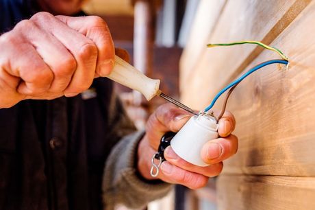 Picture of a electrical handyman services repair provider holding a white screwdriver installing a light. The wall has a blue , green, yellow and white wire connected to the light from the wall.
