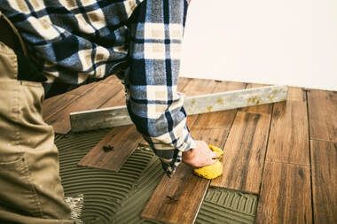 Laminate floor installation picture of a handyman installing brown hardwood holding a level and wet sponge.