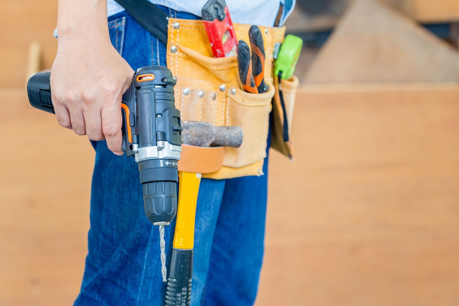 A man is holding a drill and a hammer while wearing a tool belt.