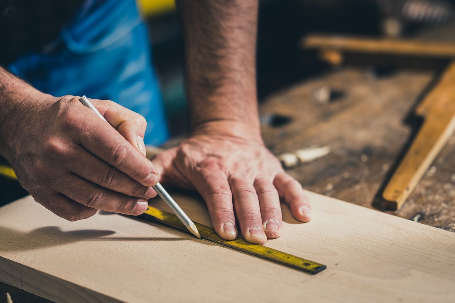 A man is measuring a piece of wood with a ruler and pencil.