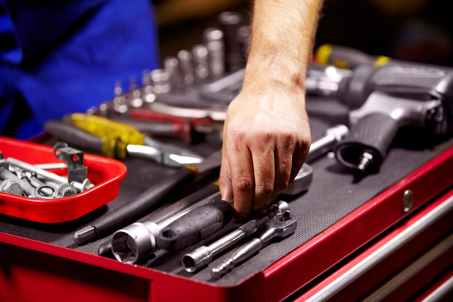 A man is reaching for a wrench in a toolbox.