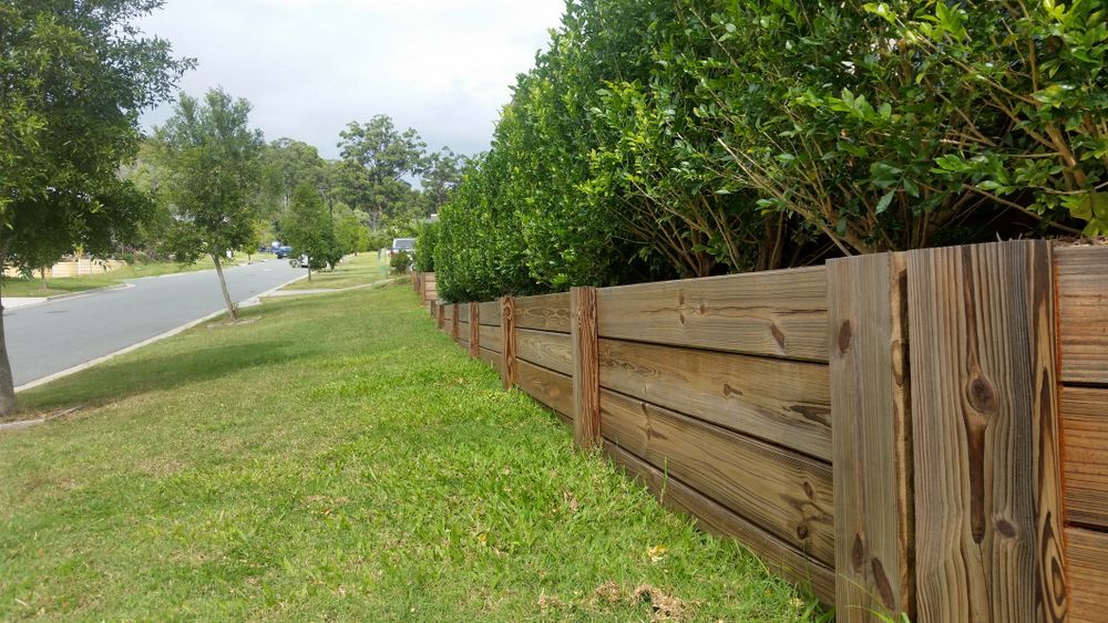 A Wooden Fence Surrounds a Lush Green Field Next to a Road — Brendan's Landscaping and Fencing In Bundaberg, QLD