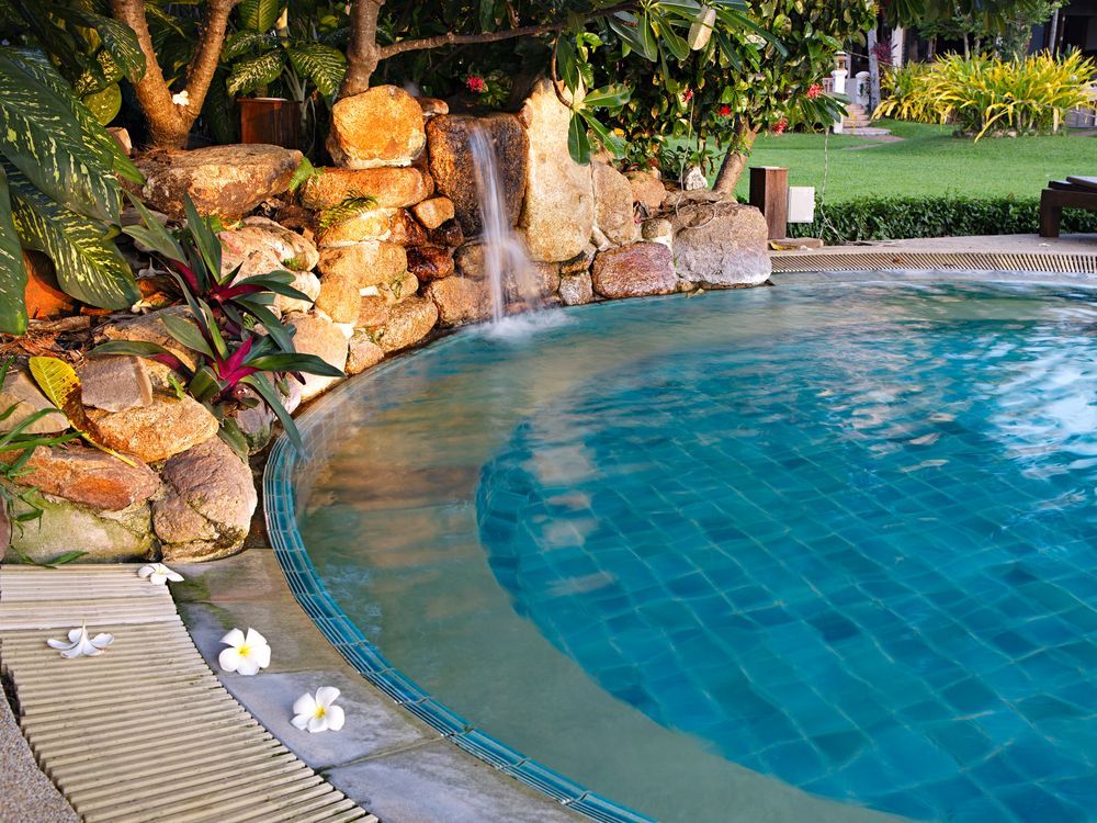 A Swimming Pool With a Waterfall in the Background — Brendan's Landscaping and Fencing In Bundaberg, QLD